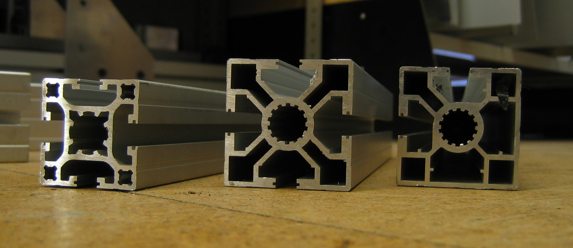 Three short pieces of extruded aluminium T-slot profile showing grooved faces and cut ends